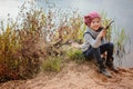 Adorable smiling child girl sitting with stick on river side with sand beach Royalty Free Stock Photo