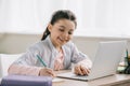 Smiling child writing in copy book and using laptop while doing homework Royalty Free Stock Photo