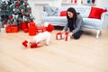 Adorable smiling infant crawling on the parquet to the christmas gifts near his mom which sits on the floor. Royalty Free Stock Photo