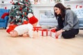 Adorable smiling infant crawling on the parquet to the christmas gifts near his mom which sits on the floor. Royalty Free Stock Photo