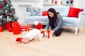 Adorable smiling infant crawling on the parquet to the christmas gifts near his mom which sits on the floor. Royalty Free Stock Photo