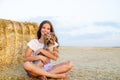 Adorable smiling little girl child sitting on a hay rolls in a wheat field with her small dog pet yorkshire terrier Royalty Free Stock Photo