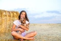 Adorable smiling little girl child sitting on a hay rolls in a wheat field with her small dog pet yorkshire terrier Royalty Free Stock Photo