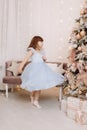 Adorable smiling little girl in festive princess blue dress is looking in camera in cozy room decorated lighting
