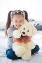 Adorable smiling littlegirl sitting on a bed hugging a white teddy bear