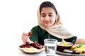 Adorable smiling Pakistani Muslim girl with beautiful eyes sitting at kitchen table, kid with hijab holding date fruit, enjoy Royalty Free Stock Photo