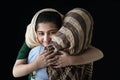 Adorable smiling Pakistani Muslim girl with beautiful eyes wearing hijab, hugging her mother on dark black background, warm love