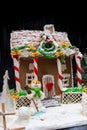 Adorable snow-covered homemade gingerbread house, a sprig of Christmas tree and a sugar mastic snowman on dark background Royalty Free Stock Photo