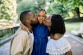 Adorable summer portrait of young african family of three posing together outdoors in beautiful park. Lovely parents are