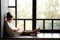 Adorable teenage girl sitting on a window sill, looking outside through the window. Royalty Free Stock Photo