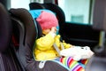 Adorable tired crying baby girl in colorful clothes sitting in car seat. Toddler child in winter clothes going on family