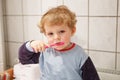 Adorable toddler with blue eyes and blond hair brushing his teeth.