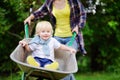 Adorable toddler boy having fun in a wheelbarrow pushing by mum in domestic garden Royalty Free Stock Photo