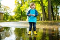 Adorable toddler boy wearing yellow rubber boots playing in a a puddle on sunny autumn day in city park. Child exploring nature. Royalty Free Stock Photo