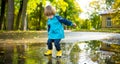 Adorable toddler boy wearing yellow rubber boots playing in a a puddle on sunny autumn day in city park. Child exploring nature. Royalty Free Stock Photo