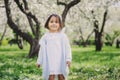 Adorable toddler child girl in light blue dressy outfit walking and playing in blooming spring garden