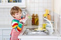 Adorable toddler child washing dishes in domestic kitchen. Royalty Free Stock Photo