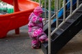 Adorable toddler climbs the stairs on the playground. toddler baby dressed in a snowsuit. autumn or winter, cold season