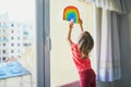 Adorable toddler girl attaching drawing of rainbow to window glass Royalty Free Stock Photo