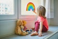 Adorable toddler girl attaching drawing of rainbow to window glass Royalty Free Stock Photo