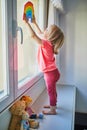 Adorable toddler girl attaching drawing of rainbow to window glass Royalty Free Stock Photo