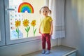 Adorable toddler girl attaching drawing of rainbow to window glass as sign of hope Royalty Free Stock Photo