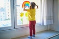 Adorable toddler girl attaching drawing of rainbow to window glass as sign of hope Royalty Free Stock Photo