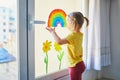 Adorable toddler girl attaching drawing of rainbow to window glass as sign of hope Royalty Free Stock Photo