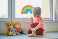Adorable toddler girl attaching drawing of rainbow to window glass Royalty Free Stock Photo