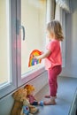 Adorable toddler girl attaching drawing of rainbow to window glass Royalty Free Stock Photo