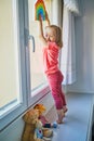 Adorable toddler girl attaching drawing of rainbow to window glass Royalty Free Stock Photo