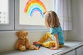 Adorable toddler girl drawing rainbow on window glass