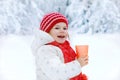 Adorable toddler girl drinking hot chocolate in winter forest. Happy healthy child with cup of steaming cocoa or tea
