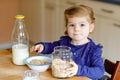 Adorable toddler girl eating healthy oatmeals with milk for breakfast. Cute happy baby child in colorful clothes sitting