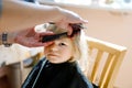 Adorable toddler girl getting his first haircut. Happy cute child sitting at the barbershop. Hairdresser making a hair Royalty Free Stock Photo