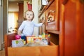 Adorable toddler girl at home, opening the drawer in the kitchen