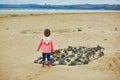 Adorable toddler girl playing with stones and building a town on the sand beach Royalty Free Stock Photo