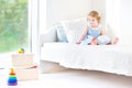 Adorable toddler girl reading book sitting on white bed Royalty Free Stock Photo