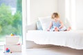 Adorable toddler girl reading book sitting on white bed Royalty Free Stock Photo