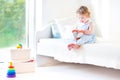 Adorable toddler girl reading book sitting on white bed Royalty Free Stock Photo