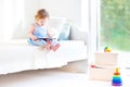 Adorable toddler girl reading a book sitting on a white bed Royalty Free Stock Photo