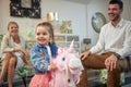 Adorable toddler girl riding a pink unicorn rocking horse in a fruniture shop with her parents sitting beside her, laughing from