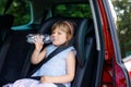 Adorable toddler girl sitting in car seat, holding bottle with water and looking out of the window on nature and traffic Royalty Free Stock Photo