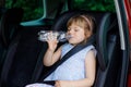 Adorable toddler girl sitting in car seat, holding bottle with water and looking out of the window on nature and traffic Royalty Free Stock Photo