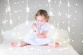 Adorable toddler girl with a toy in a white bed between Christmas lights Royalty Free Stock Photo