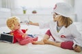 Adorable toddler girl in white coat playing doctor and giving medical care to her doll