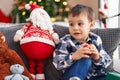 Adorable toddler holding decoration ball sitting on sofa by christmas tree at home Royalty Free Stock Photo