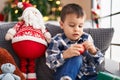 Adorable toddler holding decoration ball sitting on sofa by christmas tree at home Royalty Free Stock Photo