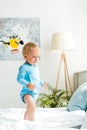 Adorable toddler kid standing on bed near laptop Royalty Free Stock Photo