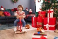 Adorable toddler playing on reindeer rocking by christmas tree at home